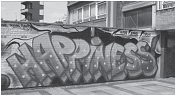 Foto de um muro grafitado com a palavra HAPPINESS em letras grandes.